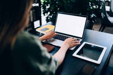 Modern işyerinin önünde parlak bir ofiste oturan ve akıllı telefon ve tabletin yanında boş ekranlı dizüstü bilgisayar kullanarak yazan tanınmamış bir kadın girişimci.