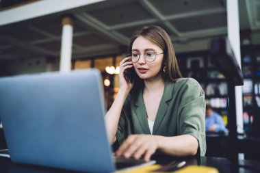 Yuvarlak gözlüklü güzel ve zeki bir kadın kütüphanede oturmuş bilgisayarın ekranına bakarken akıllı telefondan konuşuyor ve sosyal medyada geziniyor.