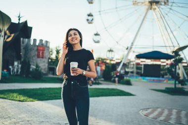 Sıradan giyinen mutlu Asyalı kadın cep telefonu cihazıyla uluslararası konuşma yapıyor. Dışarıdaki 4G 'ye bağlanıyor. Kahveli neşeli kadın lunaparkta iletişim kuruyor.