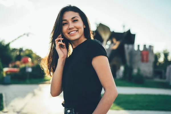 笑顔アジアのヒップスター女の子でカジュアルTシャツ笑っている間に優しいスマートフォン会話 楽しい時間の屋外での国際通信を楽しんでブルネットの髪を持つ陽気な女性 — ストック写真
