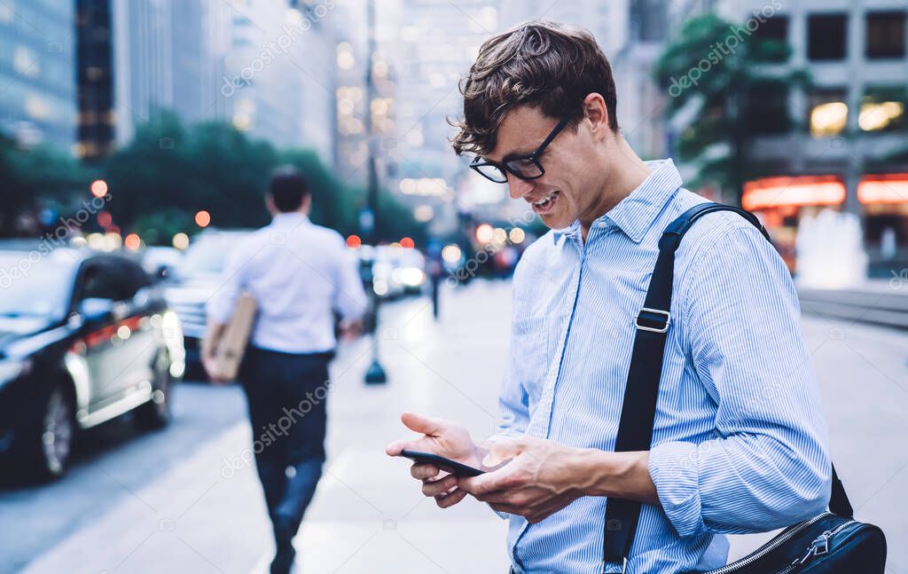 Side view of happy successful male entrepreneur reading positive sms text while chatting with friend via cellphone application, cheerful businessman formally dressed enjoying online communication