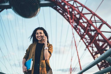 Elinde edebiyat kitapları olan gülümseyen yeniyetme kızın yarım boy portresi uluslararası mobil sohbet yaparken şehir ortamında neşeli Asyalı öğrenci cep telefonu uygulaması ile arıyor.