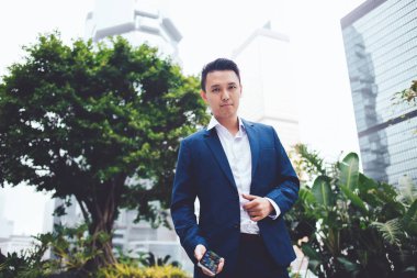 Şehir caddesinde yeşil ağaçlara bakarken elinde cep telefonu olan modern etnik girişimci modayı takip ediyor.