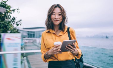 Bin yıllık Japon blogcu dijital gadegt ve kahve ile yarım boy portresi. Sanal takipçilerle iletişim kurmak için kameraya gülümsüyor. 4G kullanan kadın nesli.