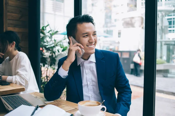 Молодой Азиатский Бизнесмен Улыбается Сидит Деревянным Столом Ноутбуком Разговаривая Смартфоне — стоковое фото