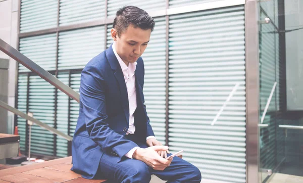 身穿蓝色正装的年轻亚洲商人坐在长椅上沉思 同时在社交网络上聊天的侧影 — 图库照片