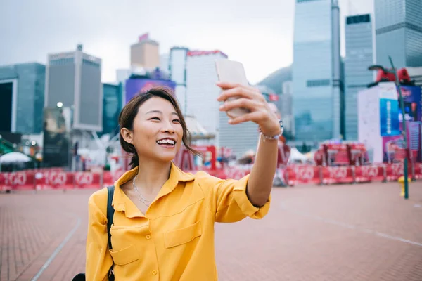 积极的年轻迷人的亚洲瘦小女性在城市里用数字智能手机拍照 同时带着摩天大楼和游乐园 面带微笑 — 图库照片