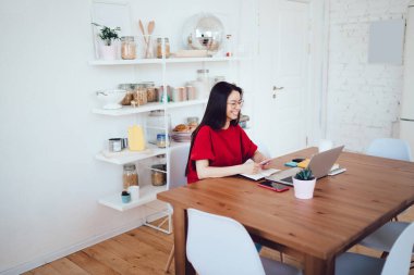 Keyifli ve neşeli bir kadın büyük ahşap bir masada dizüstü bilgisayarın önünde oturuyor ve dinlenirken gülümsüyor.