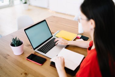 Modern kadın serbest yazar boş sayfalarla dizüstü bilgisayarın önünde oturuyor ve yazarken boş ekrana bakıyor. 