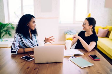 Zeki, kendine güvenen siyahi kadın ve meslektaşlarının iş arasında el kol hareketleri yaparken aydınlatma odasındaki açık laptopla yan görünümü.