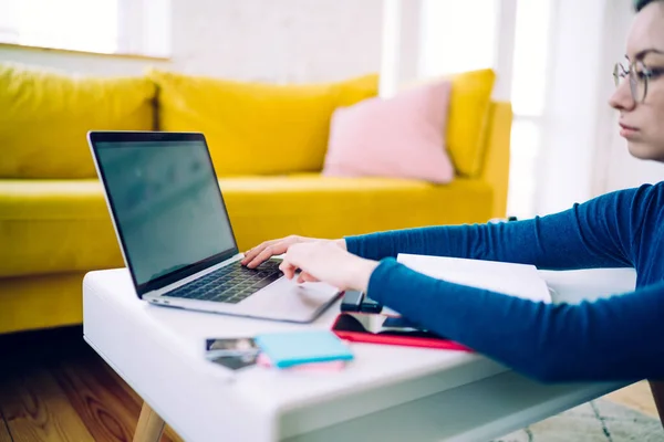 坐在地板上的戴眼镜和带灰色屏幕的冲浪笔记本电脑的休闲女性在现代家庭中遥遥领先的副景 — 图库照片