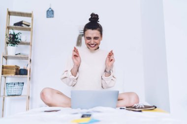 İyimser gülümseyen bayan girişimci ev tarzı giysiler içinde bacak bacak bacak üstüne atmış, gözlerini kıstırarak en iyi projenin rahat yatak odasında olmasını umuyor. 