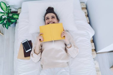 Yukardan gelen mutlu genç kadın, evde kıyafetlerini giyiyor sarı günlüğü tutuyor ve komik anları hatırlarken gülüyor. 