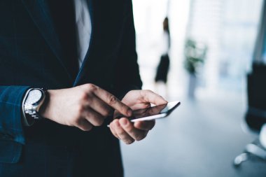 Kol saati takılı mavi takım elbiseli adam iş merkezinde siyah boş alan olan akıllı telefonları açıp kontrol ediyor.