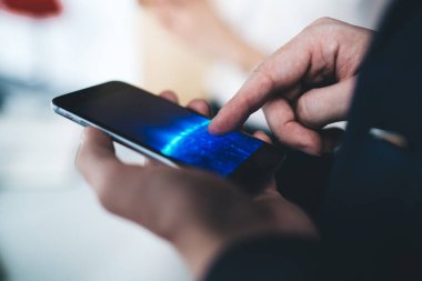 Tanımlanamayan, takım elbiseli bir erkek ofis çalışanının, dikey formatta, bulanık arka planda akıllı telefon uygulamasını kullanarak yakın plan çekimleri.