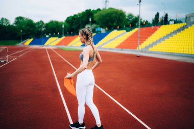 Spor giyimli, spor ayakkabılı, spor ayakkabılı, spor salonundan geçen ve mola sırasında antrenman için ekipman tutan tanınmamış zayıf bayanın yan görüntüsü.