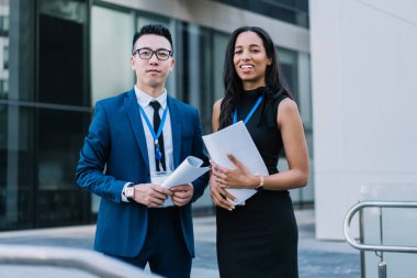Zarif giyinmiş, kimlik kartı takan ve sokaklarda elinde kağıtlarla kameraya gülümseyen neşeli kadın ve erkekler.