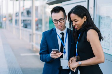 Çağdaş kadın ve erkek resmi kıyafetler ve konferans etiketleri ile şehir tren istasyonunda duran ve birlikte telefon kullanan katılımcılar. 