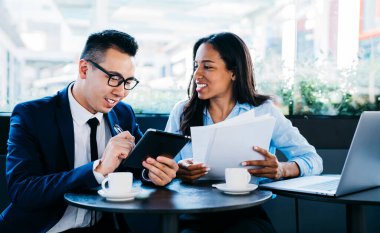 Modern genç kadın ve erkek, gazete okurken tablet kullanıyor ve kafede birlikte çalışıp kahve içiyorlar.