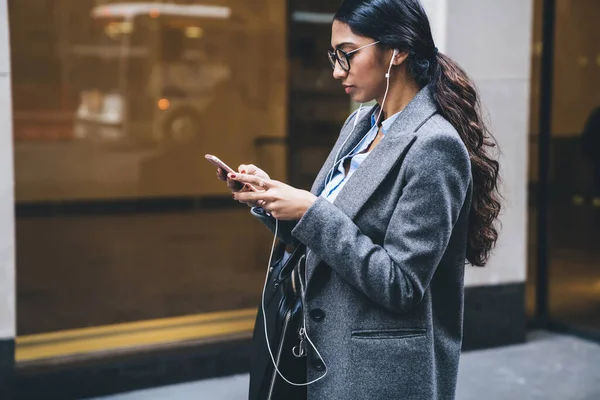 ニューヨークの街を歩きながら耳に携帯電話のヘッドフォンを置くエレガントな衣装や眼鏡を保持する民族女性 — ストック写真