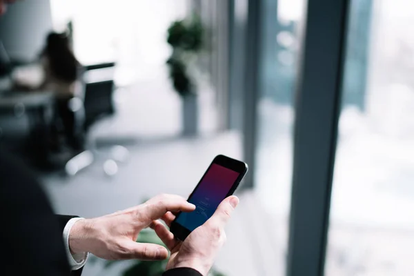 Crop side view of formal man using mobile phone app and entering credentials while working in modern office building standing on blurred background