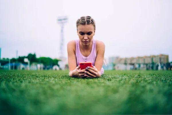 Zrelaksowana Atletyczna Kobieta Leżąca Łące Boiska Sportowego Przeglądająca Telefon Komórkowy — Zdjęcie stockowe