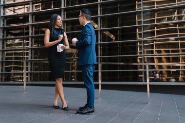 İsim etiketli kadın ve erkeğin sokakta dikilip sohbet ederken kahve içişlerinin yan görüntüsü