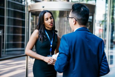 Siyah elbiseli ve isim etiketli güzel Afro-Amerikalı kadın konferansta olan ve sokakta duran erkek arkadaşla konuşuyor.