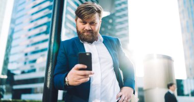 Şehir merkezinde cep telefonuyla dikilen ve kameraya bakan profesyonel döviz uzmanının yarım boy portresi, cep telefonu aletli beyaz adam dışarıda girişimci ortağı bekliyor.