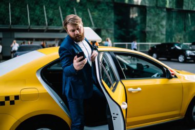 Deneyimli erkek ekonomist sarı takside oturuyor ve şirket patronu ile iş toplantısına gidiyor. Modern cep telefonu cihazıyla online para transferi yapıyor.