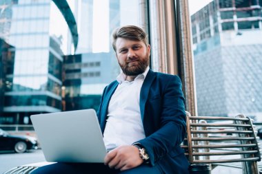 İletişim ve iş için modern dizüstü bilgisayarla şehir ortamında oturan başarılı yetenekli bir adamın portresi, e-posta bekleyen zeki girişimci