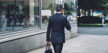 Şehir caddesinde yürüyen ve New York 'ta akıllı telefon üzerinde çalışan, modern, siyah takım elbiseli başarılı, gri saçlı iş adamının arka planı.