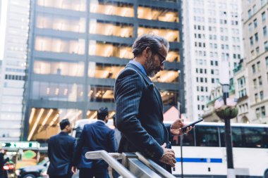 Ofisteki şık orta yaşlı adamın yan görünüşü New York 'un iş merkezinde duruyor ve cep telefonu kullanıyor.