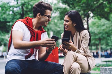 Parktaki taştan bankta oturmuş ellerinde akıllı telefonlarla birbirlerine bakan mutlu bir çift.