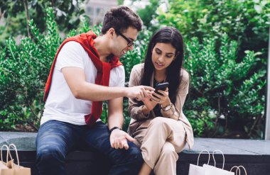 Gündüz vakti şehrin göbeğinde otururken alışveriş torbalarıyla akıllı telefonlara göz atan modern, çok ırklı genç adam ve kadın eğlendi.