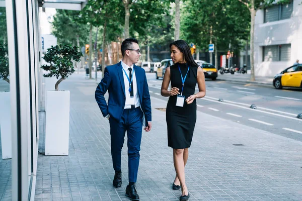 Elegant African American woman with Asian man wearing name tags and having friendly discussion while walking down street meeting on business conference