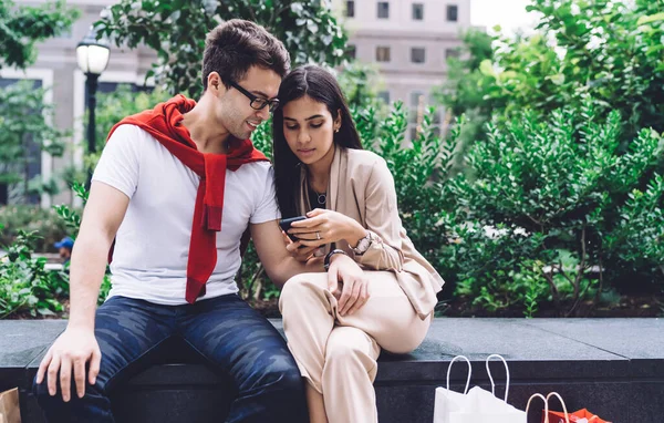 Stock image Stylish serious modern casual multiracial young man and woman browsing on smartphone while sitting on parapet on city street  in daylight