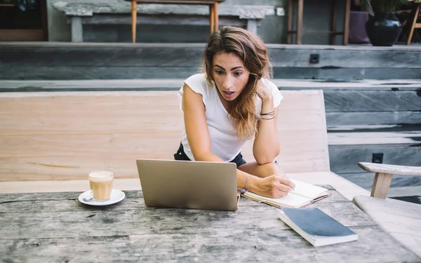 Hermosa Mujer Sorprendida Escribiendo Cuaderno Mirando Computadora Portátil Mientras Está —  Fotos de Stock