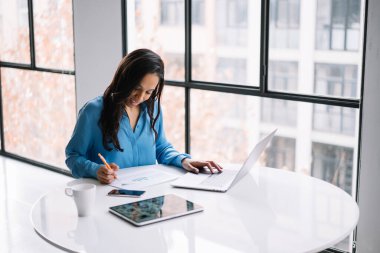 Bilgisayarda yazı yazan, ofisteki beyaz yuvarlak masada oturan bilgilerin doğruluğunu doğrulayan modern akıllı Afrikalı Amerikalı uzman.