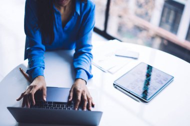 Yukarıdan yetenekli afro-amerikan iş kadını dijital dizüstü bilgisayarın klavyesine yazarak aydınlık bir pencerede oturuyor.