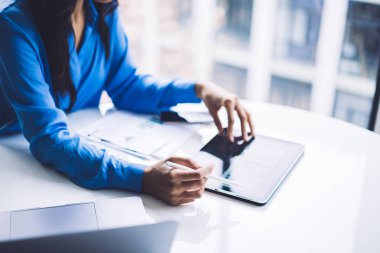 Resmi bluz giyen, tablet kullanan ve modern ofisteki beyaz yuvarlak masada doküman inceleyen Afrikalı Amerikalı kadınların seçici odak noktası. 