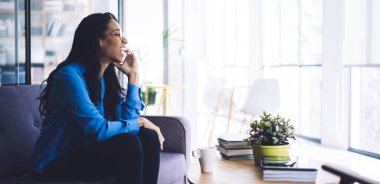 Neşeli, Afro-Amerikalı genç bir kadının aydınlık odada oturması, evini araması, başka tarafa bakması.