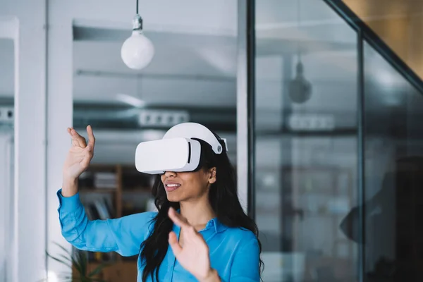 現代のヘッドセットを使用して仮想現実を経験し 事件の隣に滞在オフィスで空気中の架空のものに触れようと笑顔の女性 — ストック写真