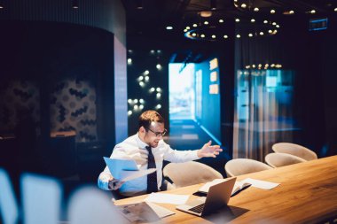 Duygusal stresli iş adamı dizüstü bilgisayar ve kağıt belgeleriyle fazla çalıştıktan sonra gergin bir ruh hali içinde, kızgın erkek ofis çalışanı başarısızlıkla sonuçlanan yeni projeler için verimli bir strateji arıyor.