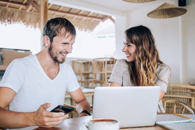 Neşeli bir adam cep telefonu ve dizüstü bilgisayar kullanıyor ve güzel bir kadın kahkahalarla kahkaha atıyor.