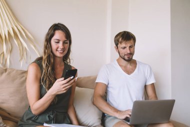 Odaklanmış yakışıklı adam dikkatle dizüstü bilgisayara bakıyor. Evdeki koltukta oturuyor. Güzel bir bayanın yanında oturuyor.