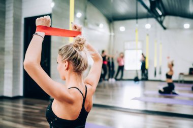 Ayna sporcusu kadının spor salonunda dizlerinin üzerinde oturan gruba spor lastiğiyle egzersiz göstermesinin arka plan görüntüsü