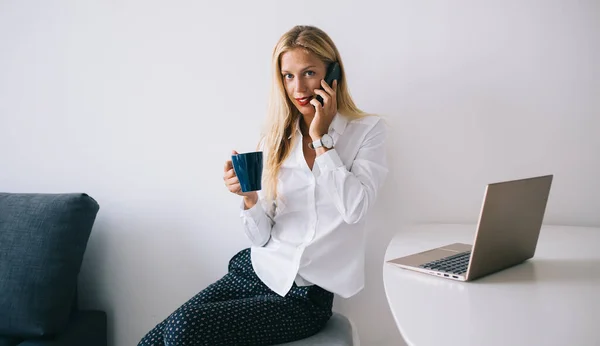 Beyaz Masada Oturan Mavi Bardağı Bluzunda Tutan Akıllı Telefondan Konuşan — Stok fotoğraf