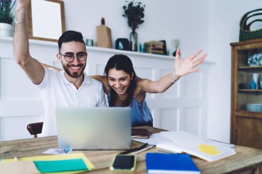 Siyah saçlı, gözlüklü, gülümseyen ve mutlu bir kadın olan erkek el kaldırıyor ve başarılı iş çıkardıkları için birbirlerini tebrik ediyor. Mutlu çift dizüstü bilgisayardan e-posta alıyor