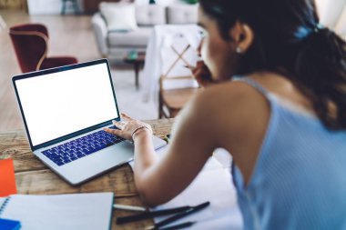 Bilgisayarda yazı yazan genç bir bayanın, ahşap masada elinde belgelerle dikilirken ve ışık odasında proje çizerken görüntüsü.